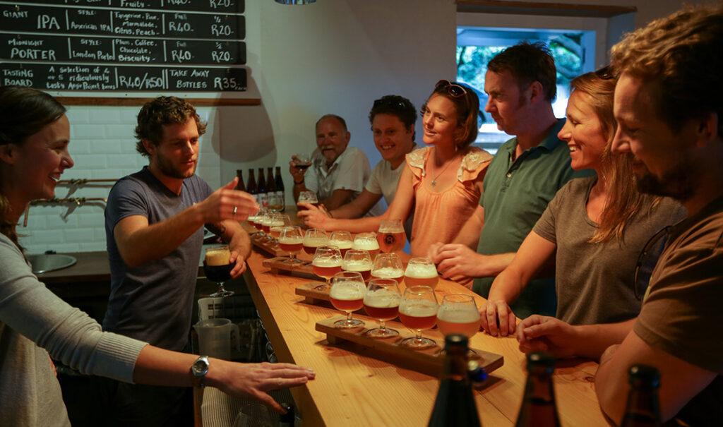 Group of friends enjoying a craft beer tasting together at a wooden communal table.