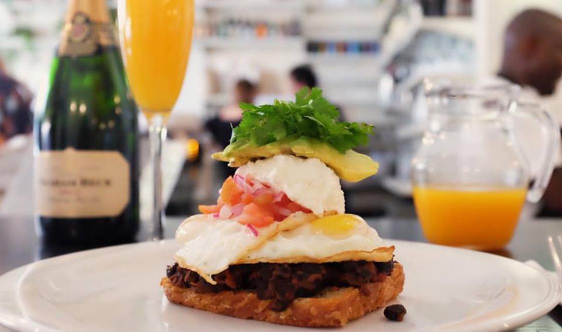 Breakfast spread at Clarke's Dining, featuring a burger, orange juice, and a glass of bubbly.