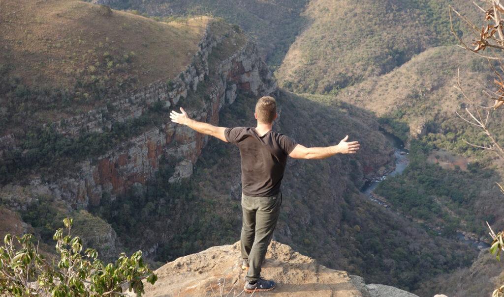 Man stretches his arms out at the top of Blyde River Canyon viewpoint.