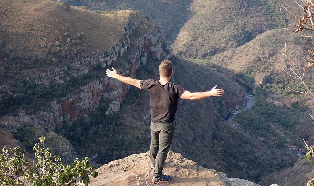 Man stretches his arms out at the top of Blyde River Canyon viewpoint.