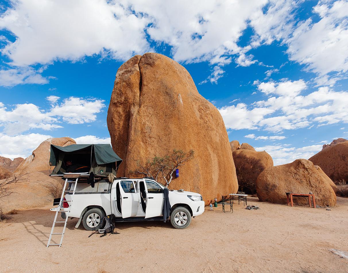 Rooftop tent set up at a camping site with rock formations in the background.