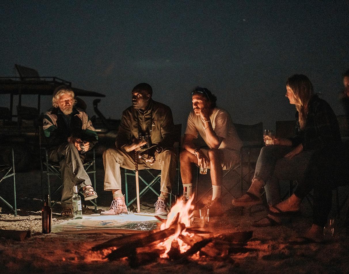 Group of travellers gathered around a campfire at night.