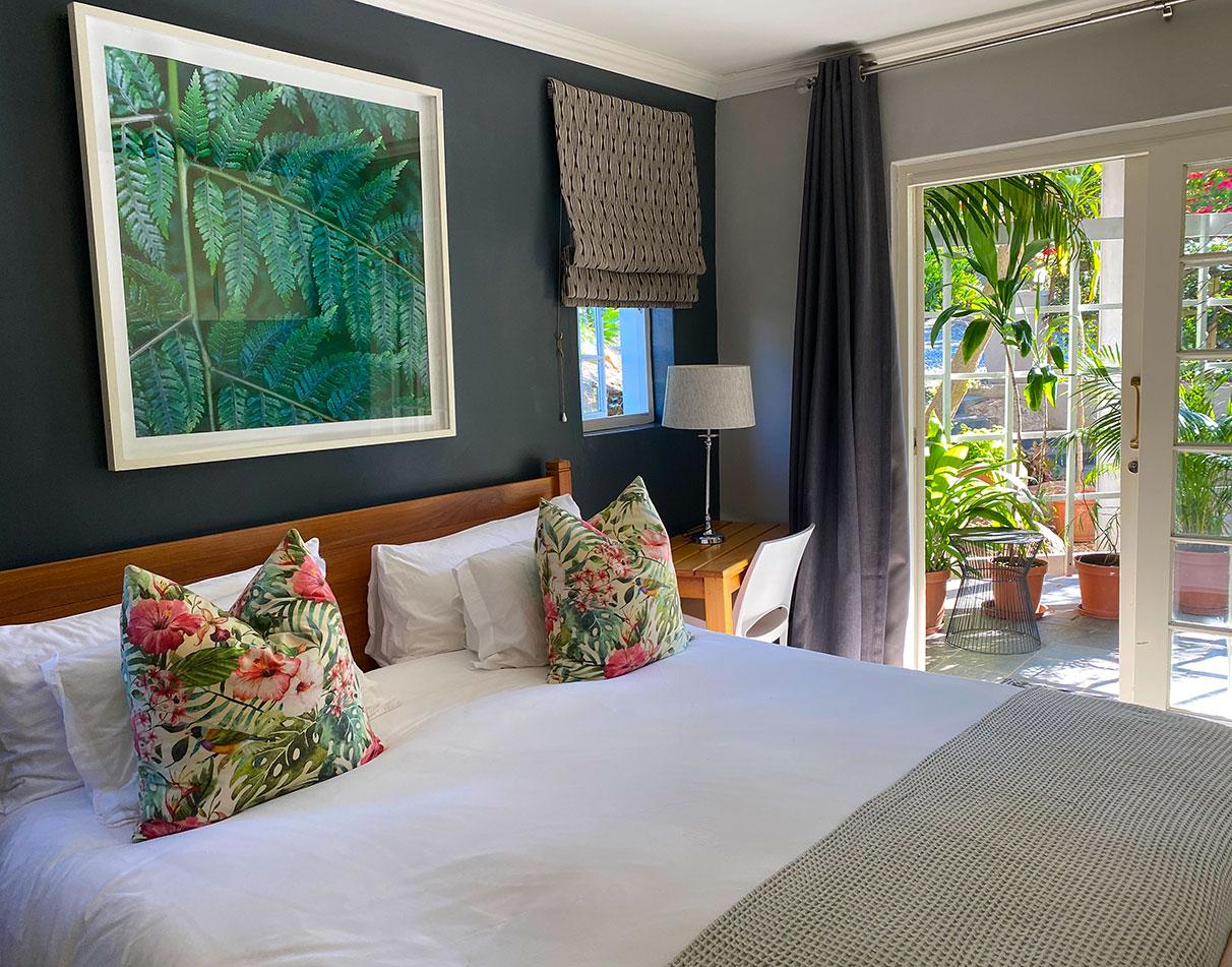 A double room at Mogi Boutique Hotel with tropical decor, floral cushions and French doors opening onto a garden.