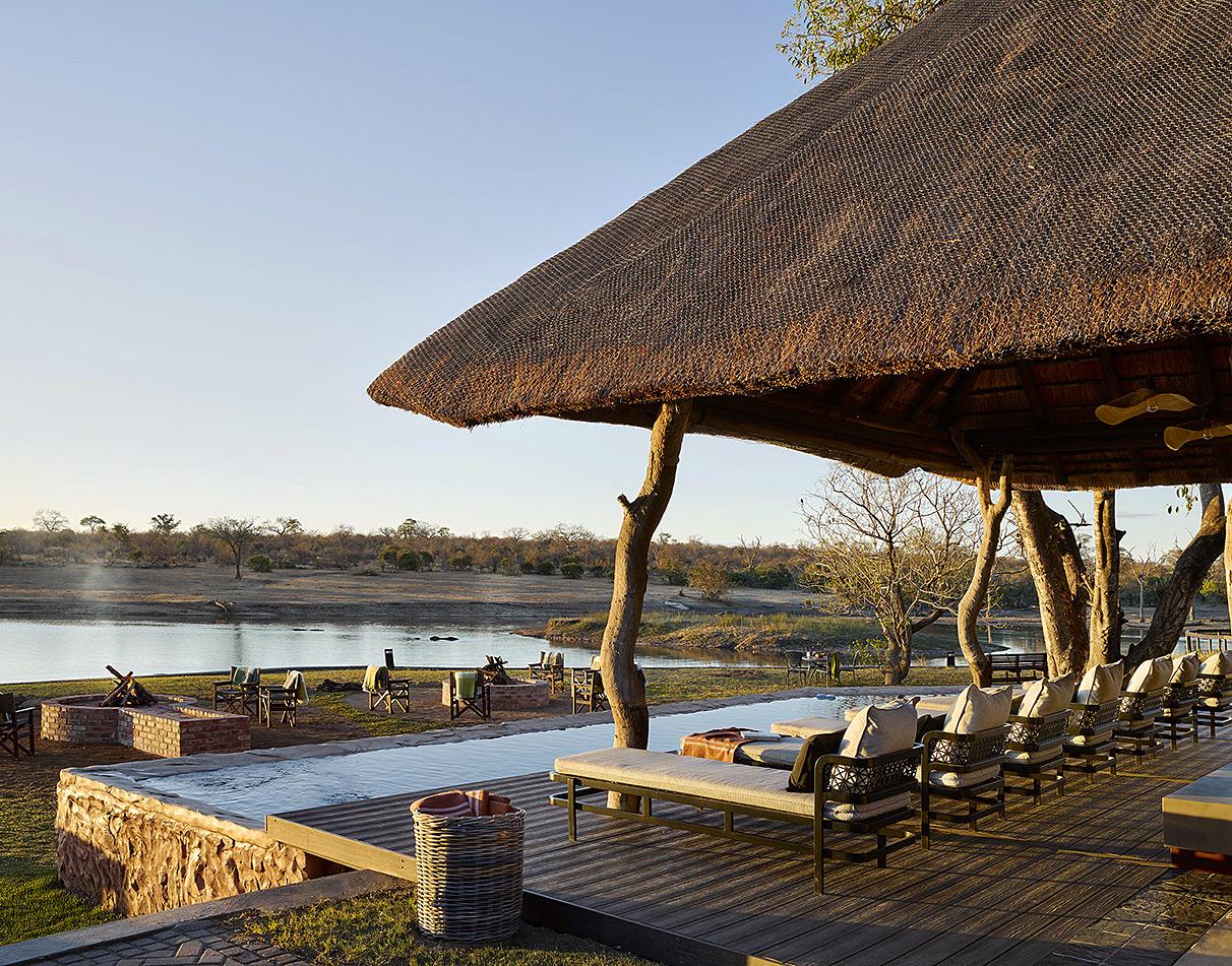 Arathusa Safari Lodge thatched veranda with pool and sun loungers overlooking the waterhole and river at golden hour.