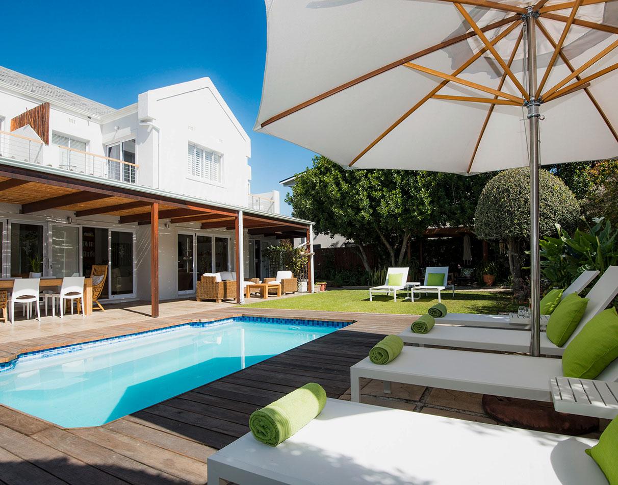 Bamboo Guest House pool and garden with sun loungers, wooden deck and lush greenery under a blue sky.