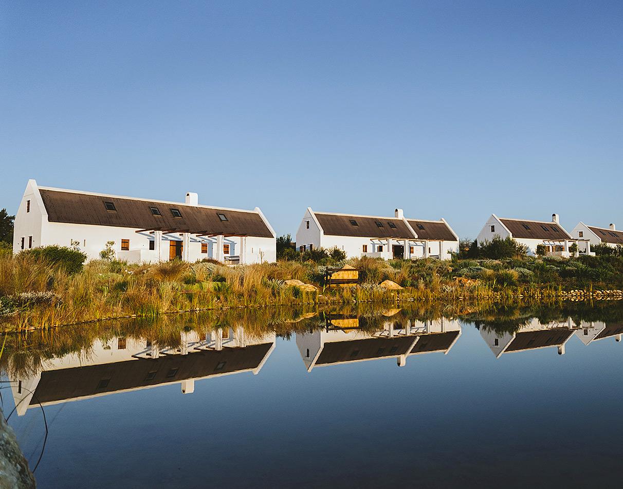Babylonstoren farm cottages with white Cape Dutch facades reflected in a still lake.