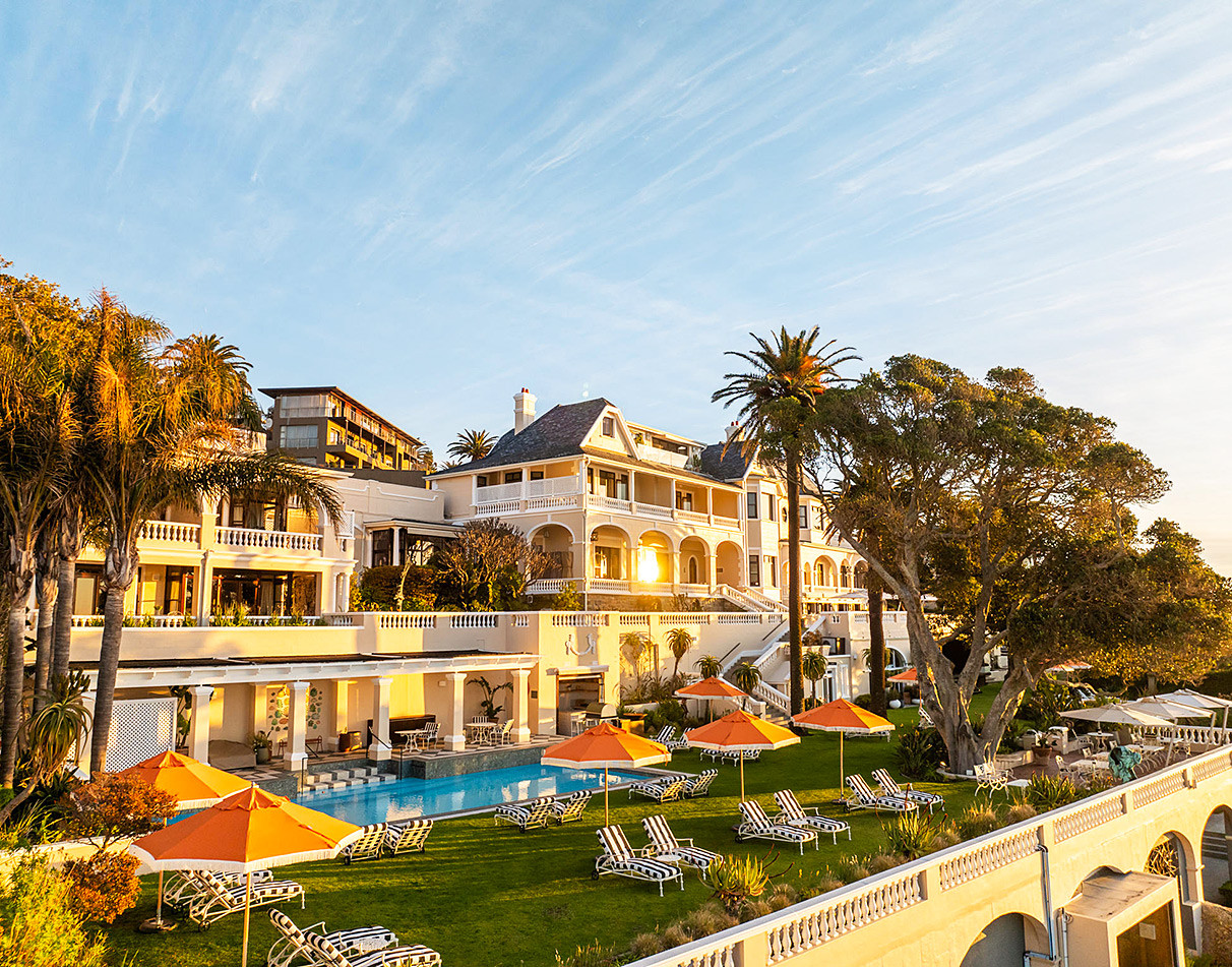 Historic Ellerman House mansion with pool terrace and palm trees at golden hour, Cape Town.
