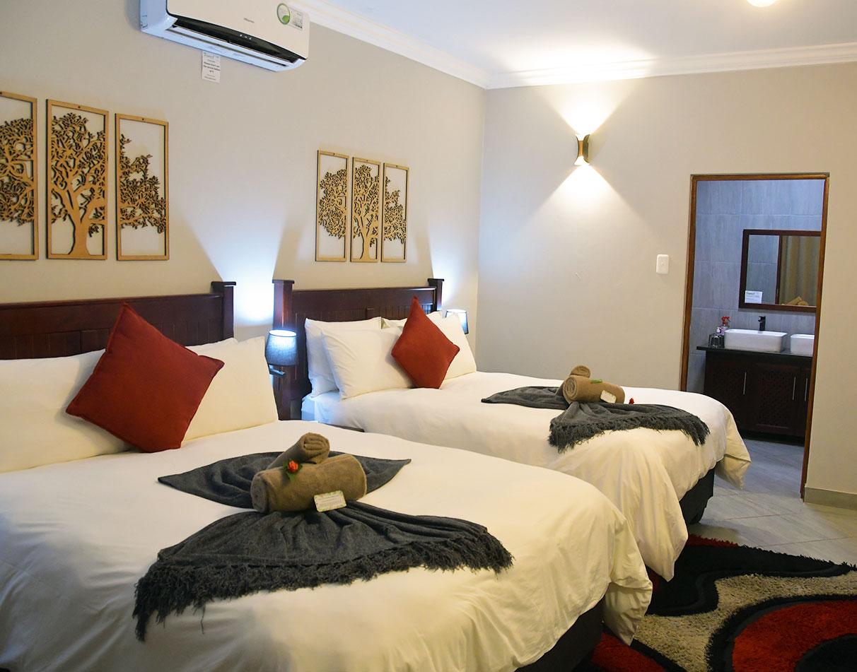 A twin room with white linen, red cushions, wooden tree wall art, and an en-suite bathroom at Forest Lodge.