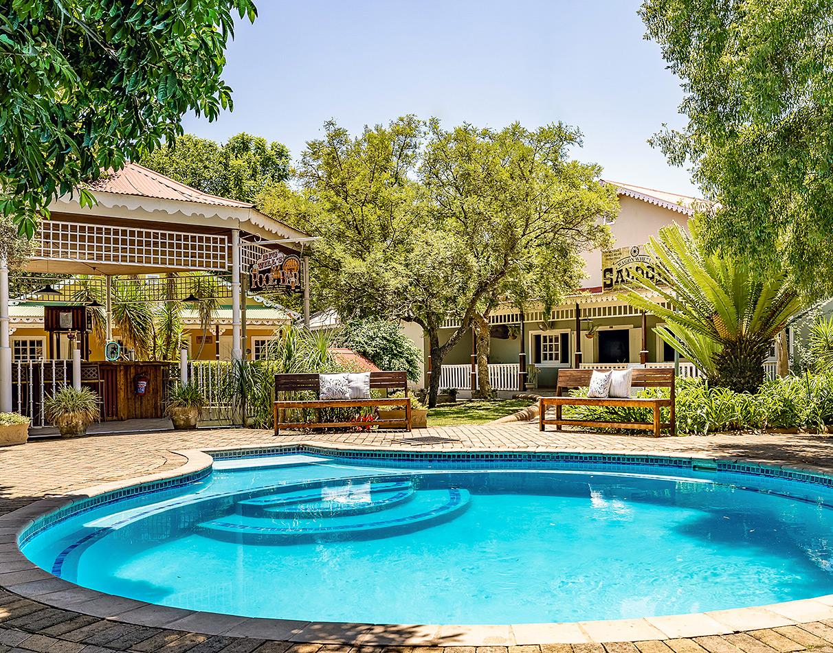 Swimming pool surrounded by lush gardens and a Wild West-themed saloon at Hotel Numbi, South Africa.