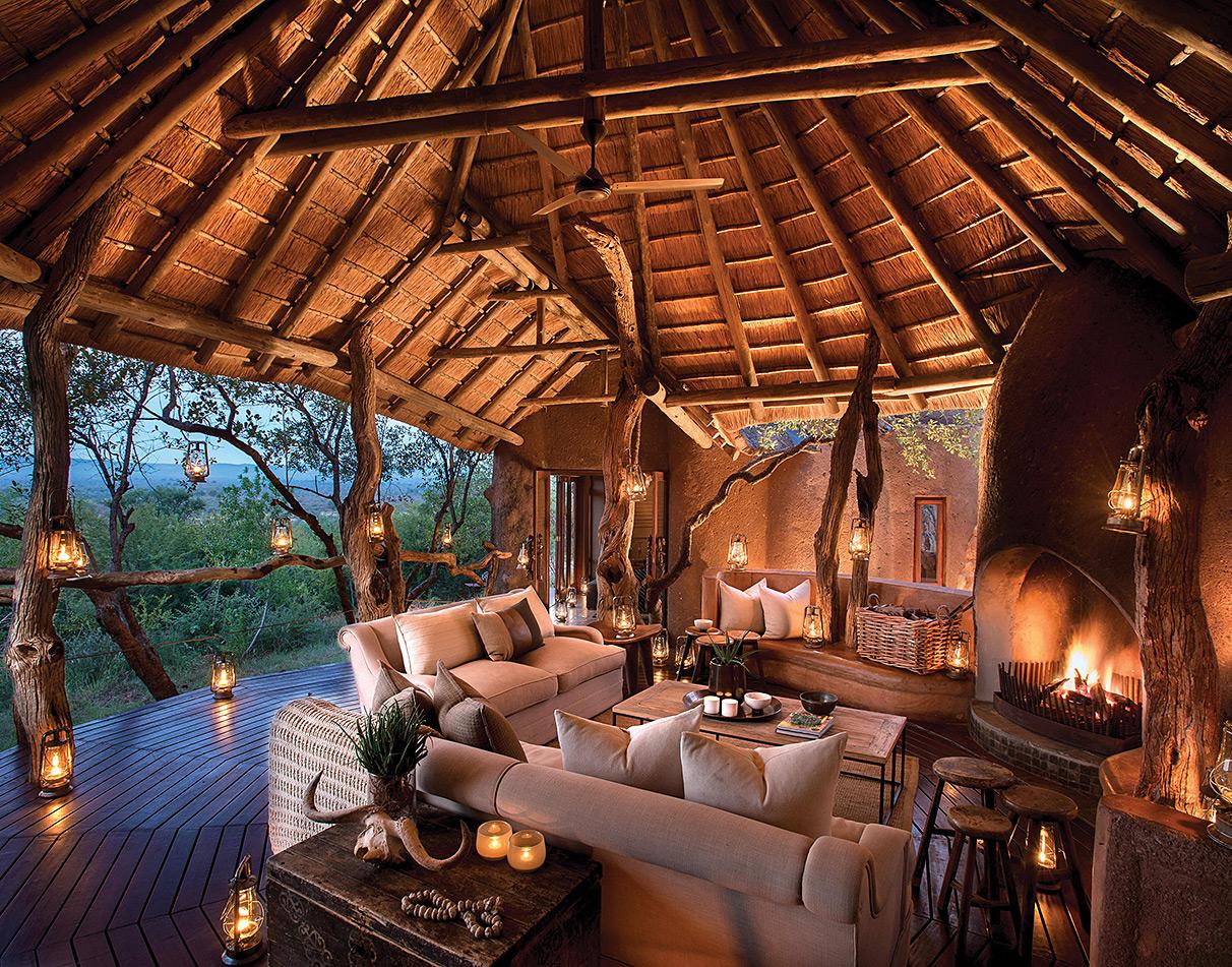 Madikwe Safari Lodge communal area at evening with lantern-lit thatched lounge, roaring fireplace and open bush views.