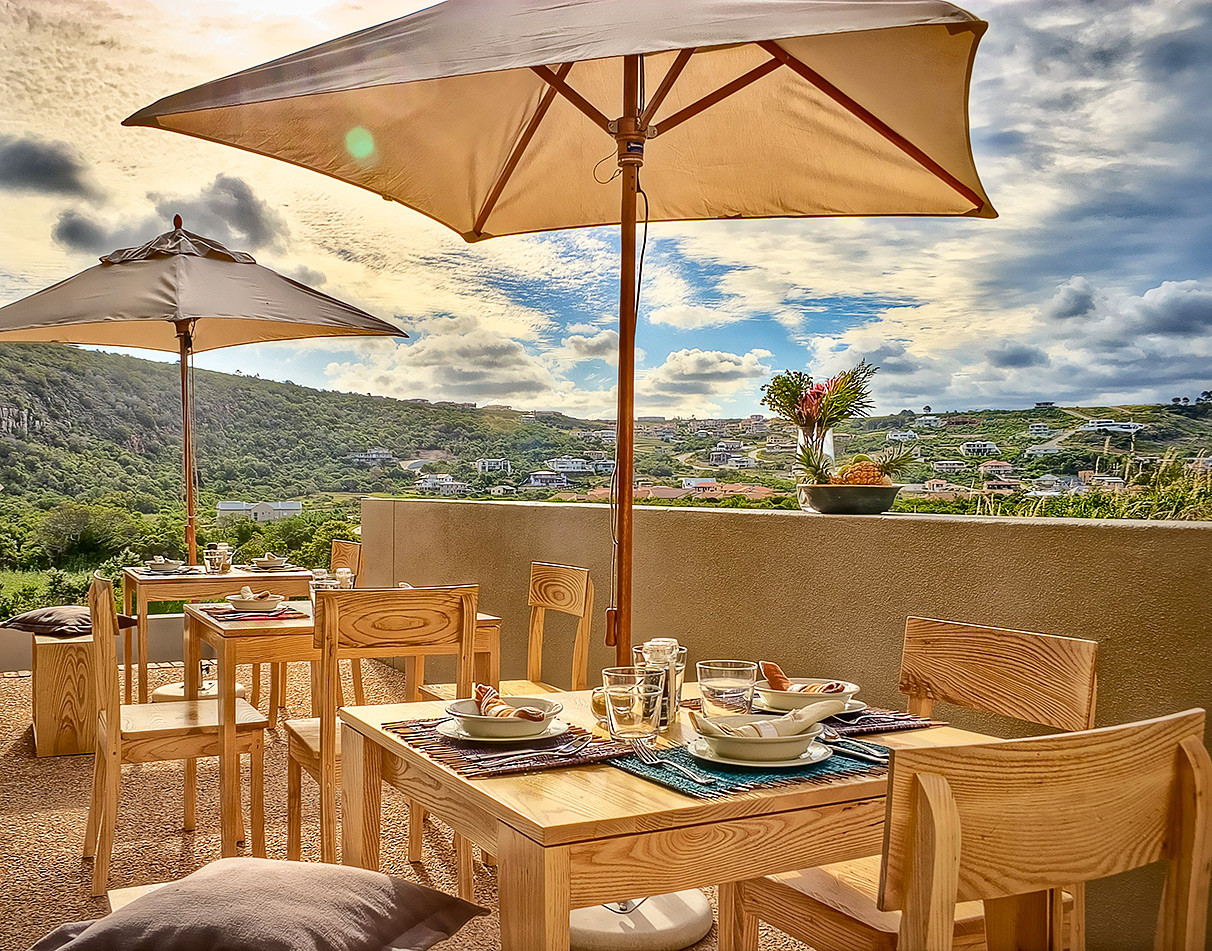 Restaurant veranda with tables, chairs and umbrellas at the Christiana Lodge in Plettenberg Bay, South Africa.