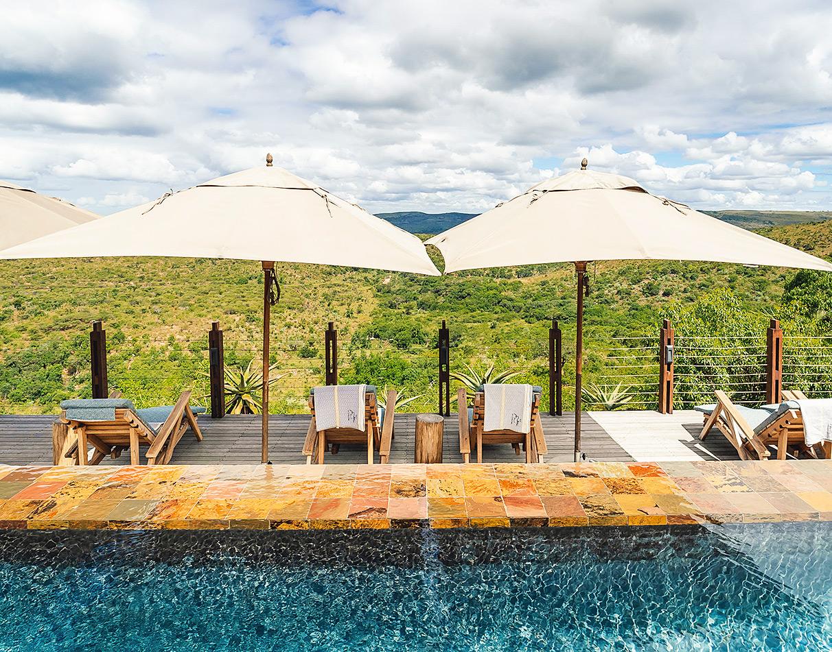 Rhino Ridge Safari Lodge pool deck with sun loungers and umbrellas overlooking the Hluhluwe valley.