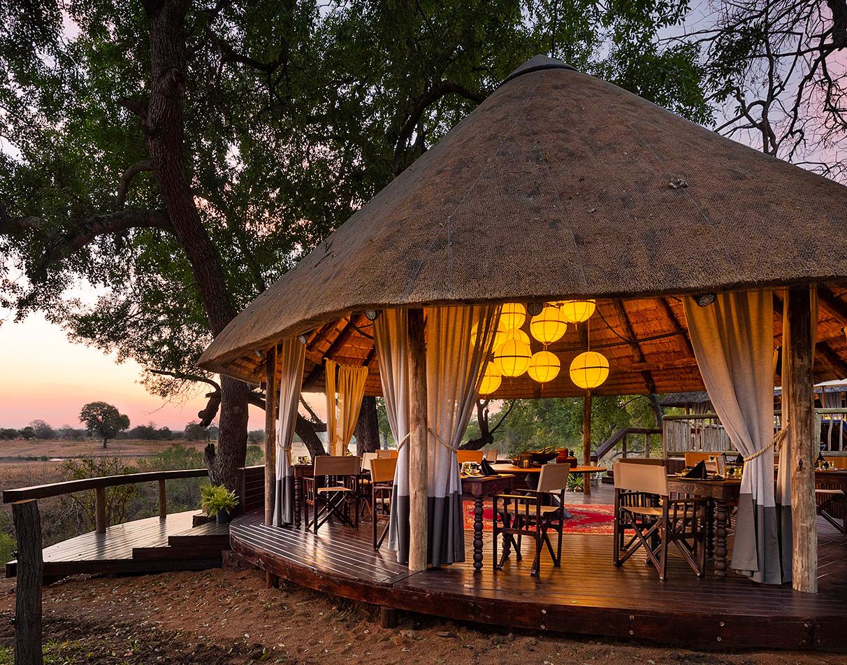 Sabi Sabi Selati Camp open-air thatched dining lounge with globe pendant lights and bush views at sunset.