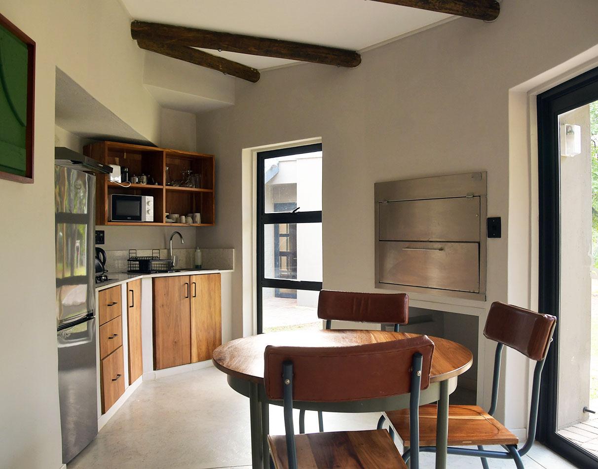 A self-catering kitchen and dining area with wooden cabinets, exposed beam ceiling at a Skukuza rest camp unit.