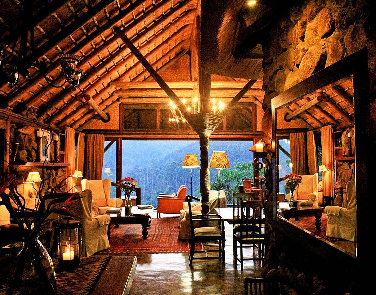 Cosy thatched lodge lounge with fireplace ambiance and forest view at Tanamera at dusk.