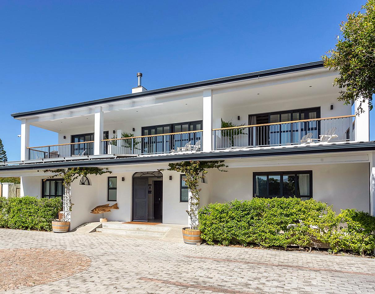Whale Rock Lodge main entrance exterior with white facade, upper balcony and cobblestone driveway.