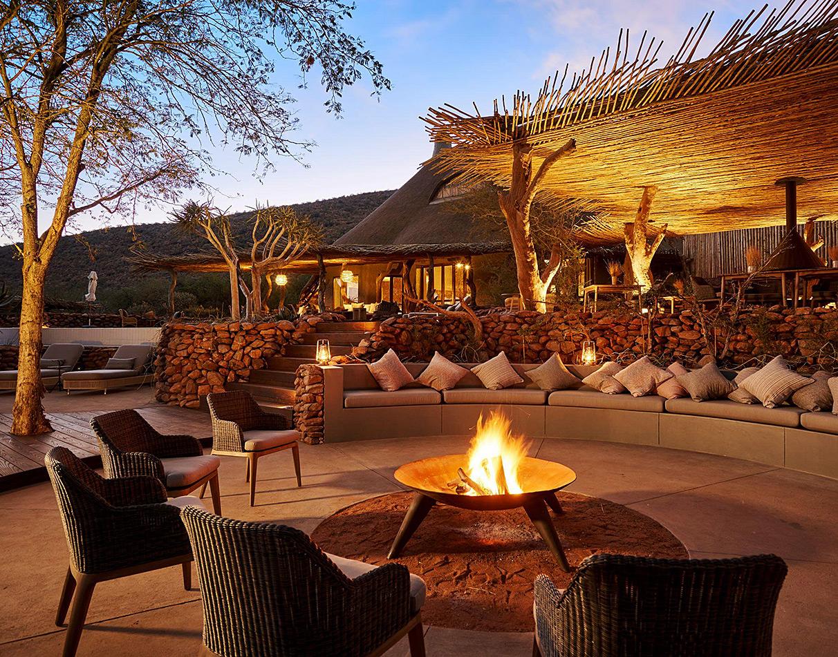 Fire place seating area at Tswalu Motse under a thatched roof at dusk.