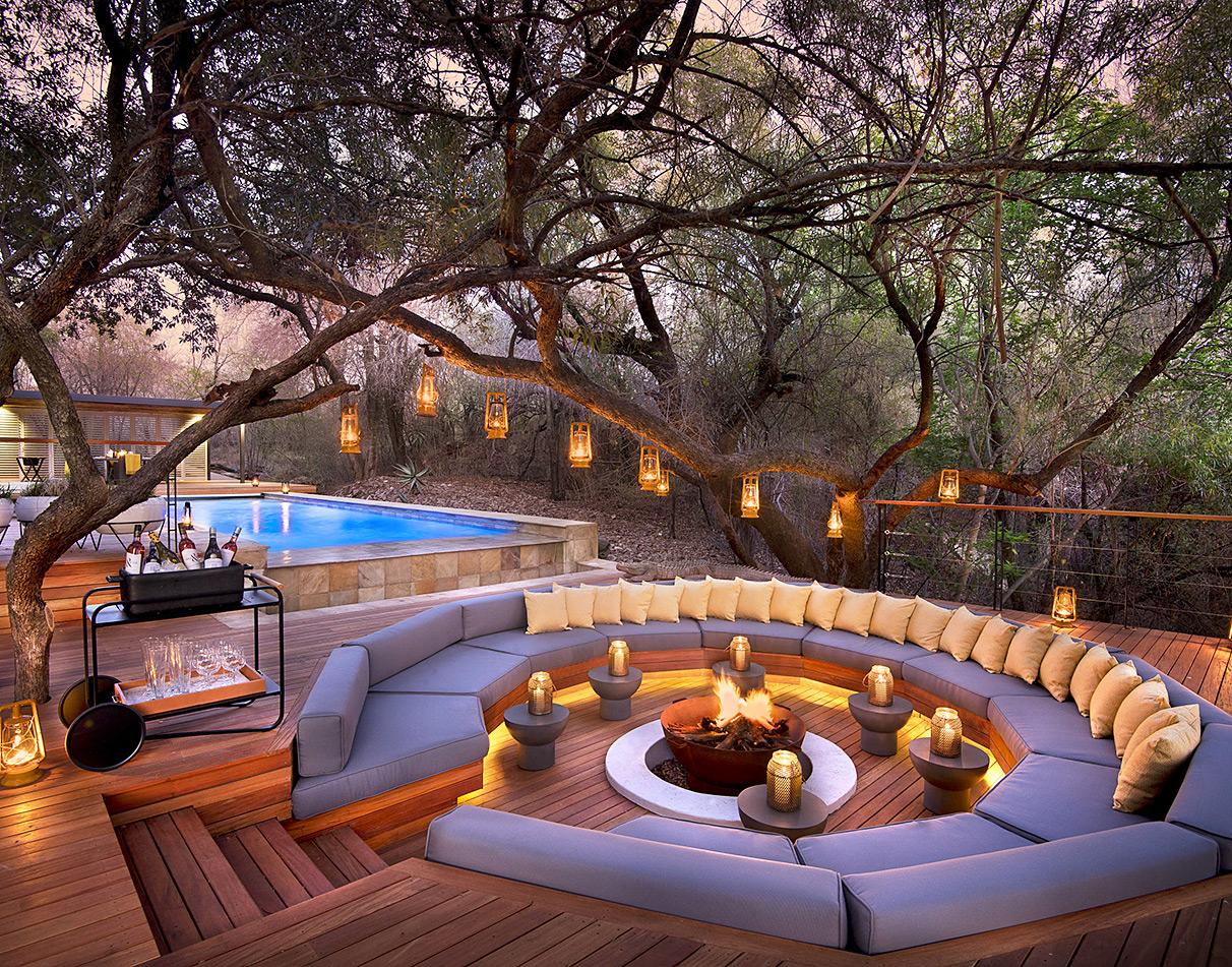 Morukuru pool deck at dusk with circular fire pit, lantern-lit trees and champagne service.