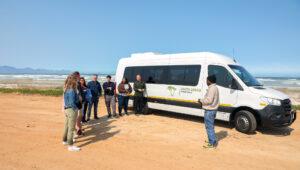 Tour guide speaks to small group by South Africa Experience van on beach.