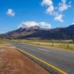 Open road cutting through the Drakensberg landscape under a blue sky.