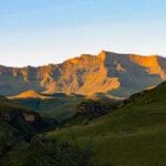 Drakensberg mountain range bathed in golden light at sunset.