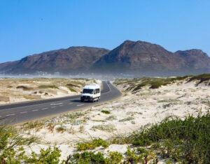 White mercedes sprinter tour vehicle driving on a coastal road near mountains in South Africa