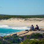 Couple sitting on a deserted West Coast beach with mountain backdrop.