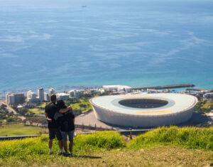 A couple hiking with views of Cape Town's coastline and stadium.