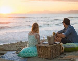 A couple enjoying a romantic picnic on the beach at sunset at Grootbos Forest Lodge, South Africa.