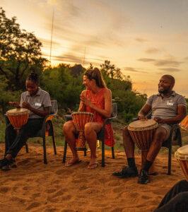Guest joining staff in an African drumming session at Royal Madikwe, a big part of South African culture at sunset.