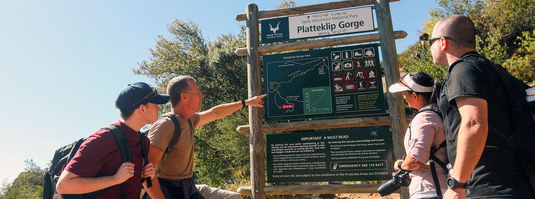 What to do in South Africa : A small group of hikers studying the trail map at the Platteklip Gorge entrance sign in Table Mountain National Park, Cape Town.