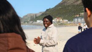 South Africa Experience guide laughing with guests on Muizenberg beach with mountain backdrop.