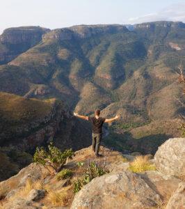 Hiker with arms outstretched overlooking the lush Blyde River Canyon, South Africa.
