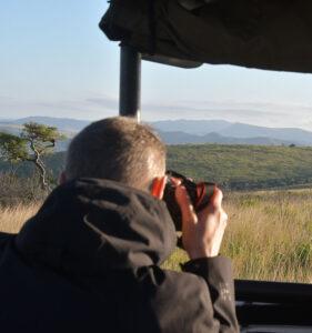 Guest on a game drive through Hluhluwe taking a photo of the landscape.