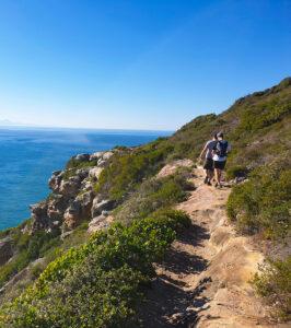 Hikers walking a coastal cliff trail with ocean views on the Garden Route, South Africa.