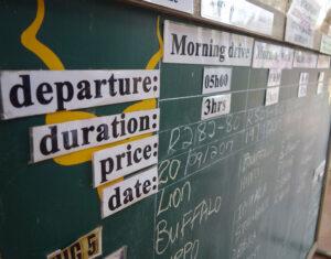 A game drive timetable board displaying departure times and prices at Kruger National Park, South Africa.