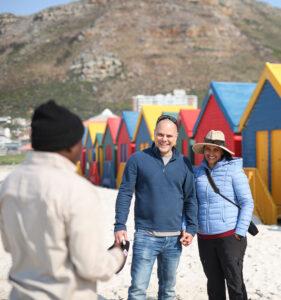 Guide talking to a couple in front of the colourful beach huts at Muizenberg beach.