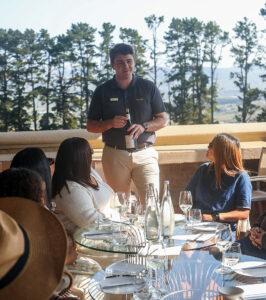 Sommelier presenting a wine bottle to guests at an outdoor tasting along Route 62, South Africa.