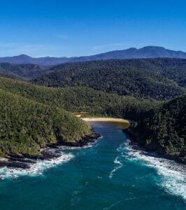 Aerial view of a hidden beach tucked between forested hills taken by Hog Hollow Country Lodge.