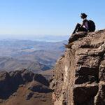 A hiker sitting on the edge of a cliff on top of the amphitheatre in the Drakensberg Mountains.
