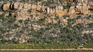 Open safari vehicle driving past rocky mountain terrain at Sanbona Wildlife Reserve.