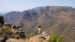 Woman standing on a rocky viewpoint overlooking the Three Rondavels and Blyde River Canyon.