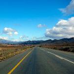 Long straight highway through South Africa's landscape with mountains in the background.