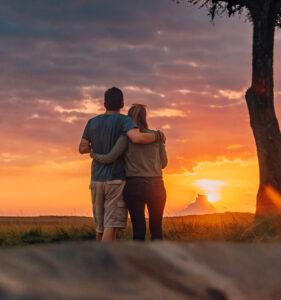 A couple hugging while looking into the sunset at a bush dinner.