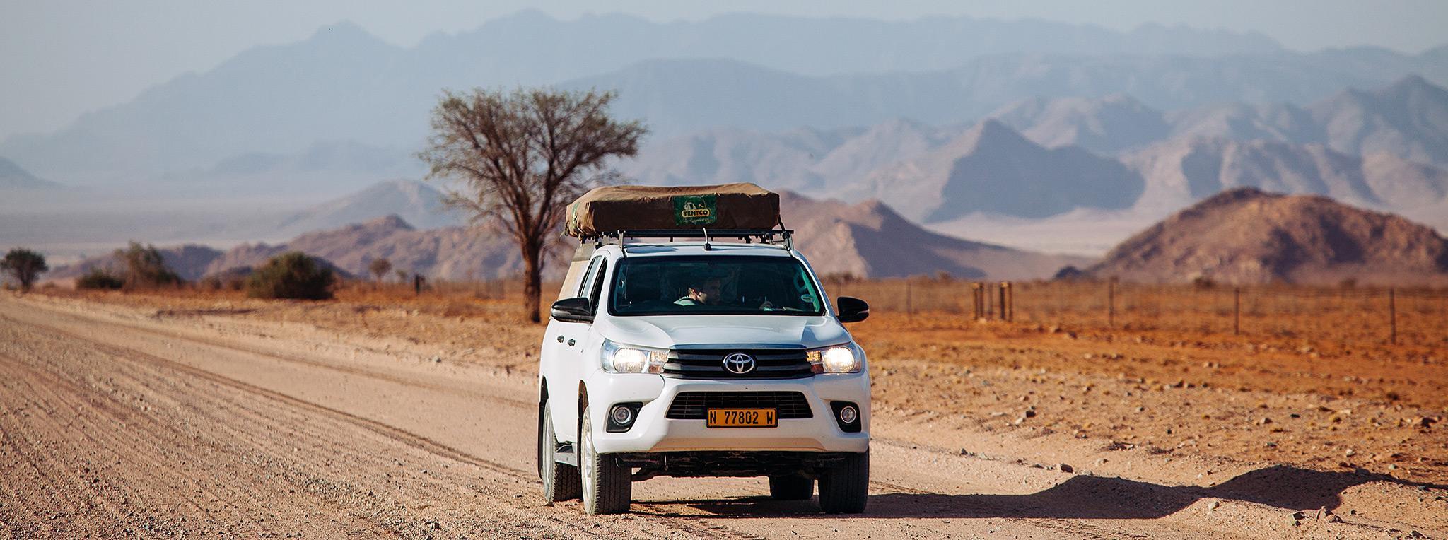 Toyota with rooftop tent on a dirt road with mountains in the background on a 4x4 self-drive tour in South Africa and Namibia.