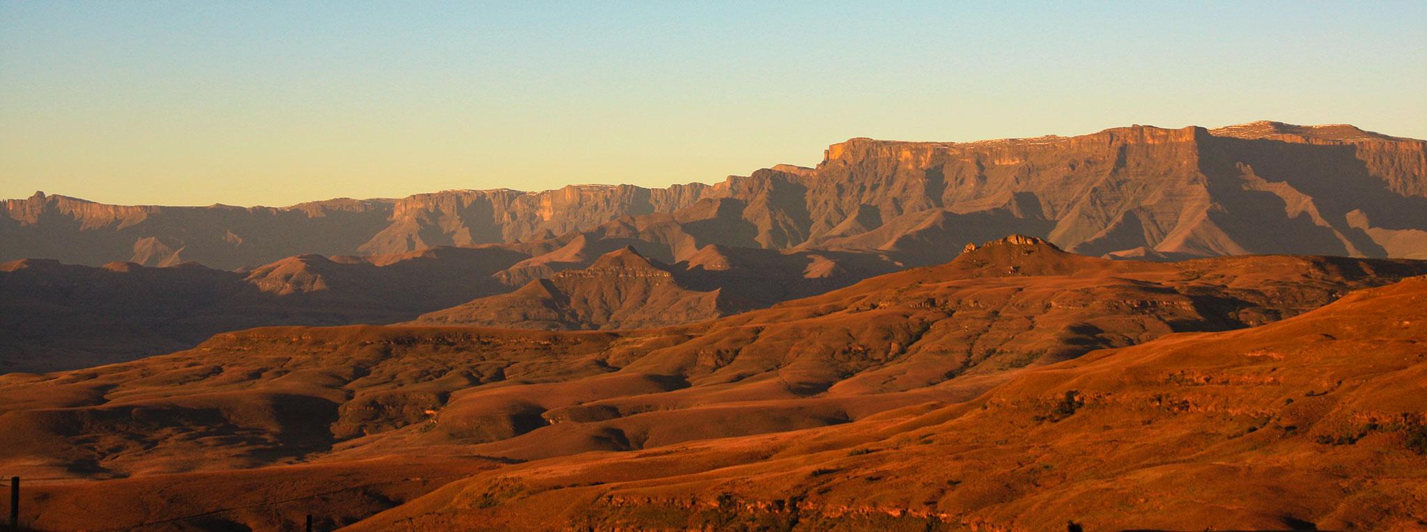 The Drakensberg mountain range bathed in warm golden light at sunrise.The Drakensberg mountain range bathed in warm golden light at sunrise.