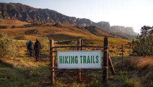 Hikers setting off on a trail past a hiking trails sign in the Drakensberg mountains.
