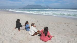 Group of friends sitting on Blouberg Beach with Table Mountain visible across the bay, Cape Town.