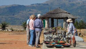 Guests browsing handcrafted African curios and sculptures at an outdoor market with mountain views.