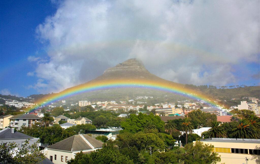 Vivid rainbow arching across Lion's Head mountain over the Cape Town suburbs.